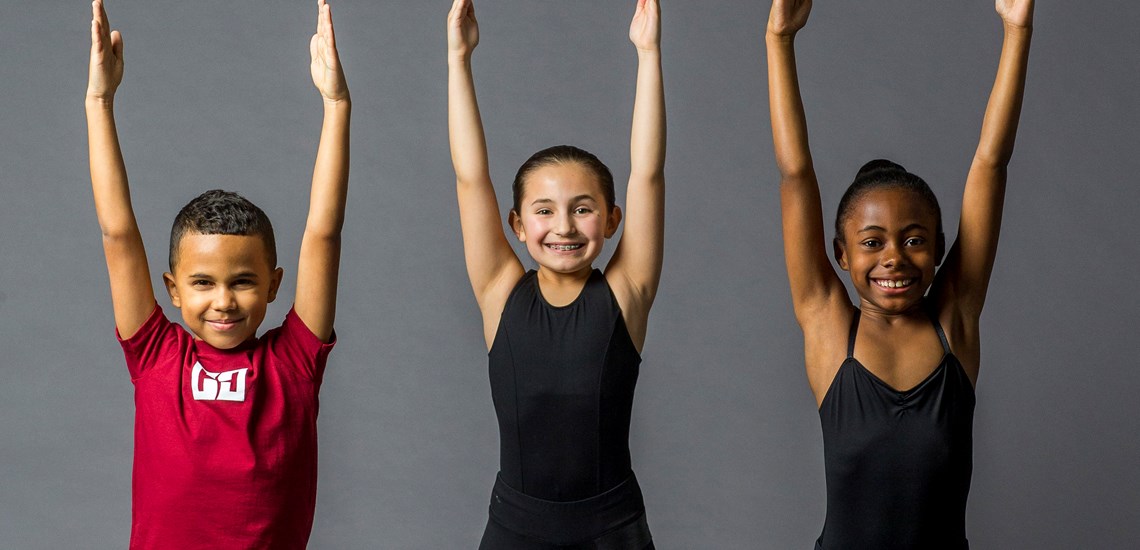 One boy and two girls in the Youth Dance Program stretching their arms above their heads.